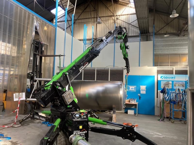 Mini grue araignée Bg Lift M250 LI vert et noir en action chez Everest Élévateurs, levant une cuve en inox à l'intérieur d'un atelier industriel, démontrant la capacité de l'équipement à manœuvrer dans des espaces restreints.